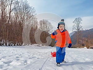 Little boy in winter outfit pull red sledge mounting the slope