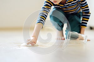 Little boy wipes water spilled from a glass on the floor. Teaching a child to clean up after himself. Responsibility, accuracy.