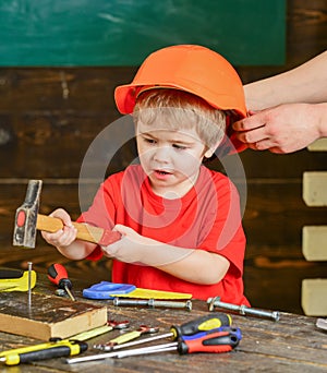 Little boy working with hammer. Daddy taking care of sons safety. Male hands holding orange protective helmet. Small kid