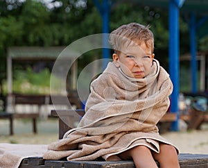 The little boy wrapped in towel for warming, sad facial expression. A little boy on the seashore.