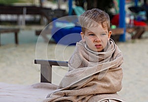 The little boy wrapped in towel for warming, sad facial expression. A little boy on the seashore.