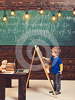 Little boy writing on chalkboard. Side view kid in front of green board with math equation. Smart little fellow studying