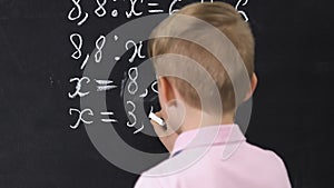 Little boy writing equation result on blackboard, school lessons, back view