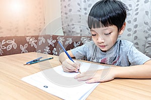 Little boy writing homework on wooden table at home. Kid learing and writing alphabet looking very happy photo