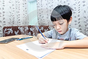 Little boy writing homework on wooden table at home. Kid learing and writing alphabet looking very happy