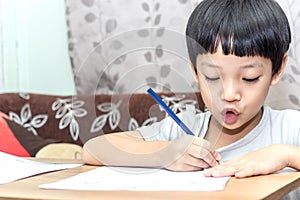 Little boy writing homework on wooden table at home. Kid learing and writing alphabet looking very happy photo