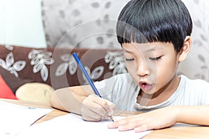 Little boy writing homework on wooden table at home. Kid learing and writing alphabet looking very happy