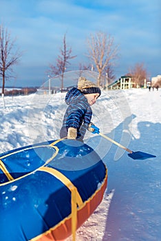 A little boy of 3 years old, in winter on street is dragging tubing, for riding from a hill, in the hands of a children