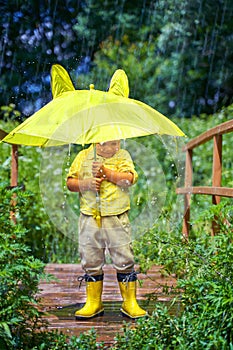 A little boy in yellow boots hides under a yellow umbrella. rain