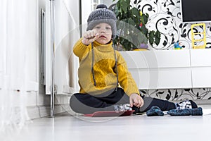 A little boy in a yellow sweater and hat is counting money and studying heating bills, near a heater with a thermostat.