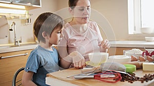 Little boy with young mother checking and weighting ingredients on digital scales. Children cooking with parents, little