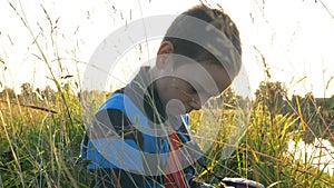 Little boyconcentrated looks at the camera screen in the grass at sunset