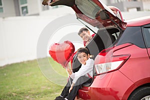 Little boys sitting on the back door of the car with balloon heart hand