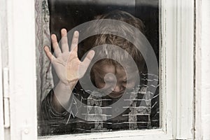 Little boystanding by the window. He is crying. The head is down. The palm on the window glass, as a symbol of farewell