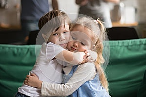 Little brother hugging upset sister sitting on couch