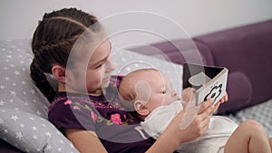 Little brother reading book with sister. Newborn baby in sister embrace