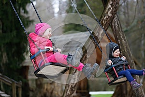 Little brother and sister laughing while having fun on a swing.