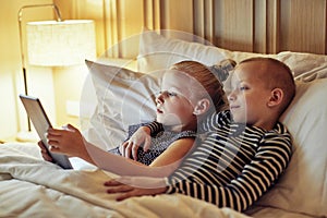Little brother and sister lying in bed watching videos together