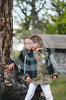 Little brother and sister standing and embracing together near the old tree trunk