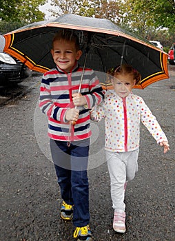 Little brother and sister under umbrella in rain