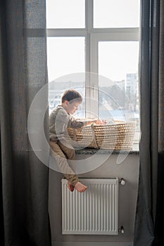 Little brother is sitting near the window with himnewborn sister in the cradle. Children with small age difference