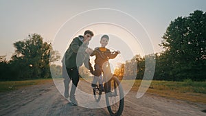 Little brother is taught to ride a two-wheeled bicycle by an older brother