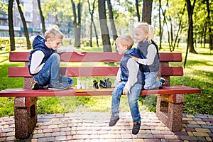 Little brothers playing chess with sister on bench in park. Children intelligence development. Family leisure time. Kids playing