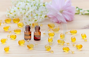 Little brown bottles with neroli and rose essential oils, gold capsules of natural cosmetic, flowers blossom on the