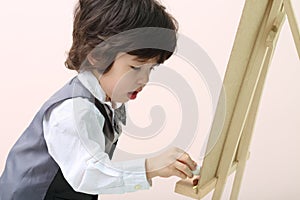 Little brunet concentrated boy draws by chalk at chalkboard