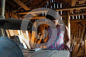 Little brunette girl in casual clothes standing among the carpentry workshop near the table with circular saw touching a