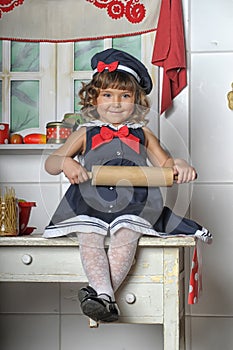 Little brunette girl with curls in a marine suit - dress  in the kitchen