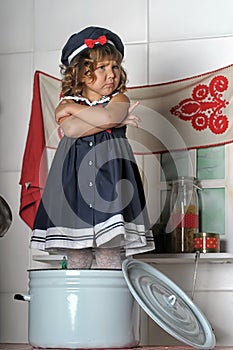 Little brunette girl with curls in a marine suit - dress  in the kitchen