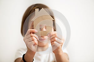 Little girl holding paper house in front of her face. Protect your home concept