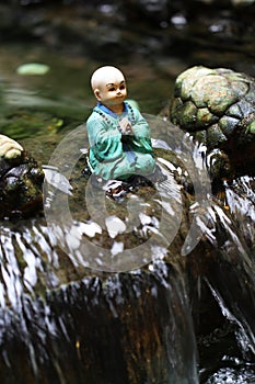 Little buddha monk statue is sitting in the middle of waterfall