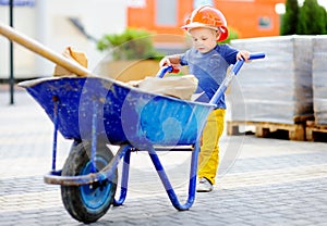 Little builder in hardhats with wheelbarrow working outdoors