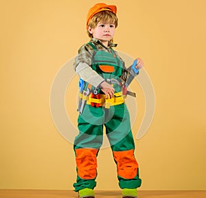Little builder in helmet and tool belt with saw. Kid repairman in protective hard hat and overalls with tool belt of toy