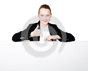 Little business woman standing behind and leaning on a white blank billboard or placard, expresses different. thumb up