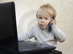 Little businessman sitting at the computer with a toy cell phone