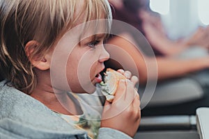 little candid kid boy five years old eats burger or sandwich food sitting in airplane seat