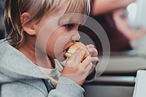 little candid kid boy five years old eats burger or sandwich food sitting in airplane seat