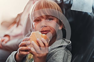 little candid kid boy five years old eats burger or sandwich food sitting in airplane seat