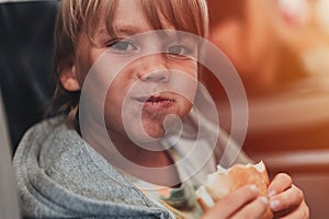 little candid kid boy five years old eats burger or sandwich food sitting in airplane seat