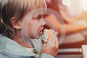 little candid kid boy five years old eats burger or sandwich food sitting in airplane seat