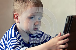 Little caucasian baby boy uses a tablet, seeing to the screen. Children time spending, computerization of youngsters.