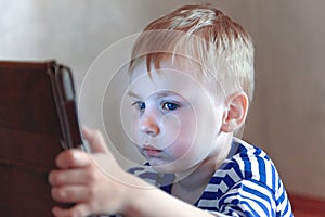 Little caucasian baby boy uses a tablet, seeing to the screen. Children time spending, computerization of youngsters.