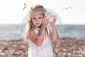 Little caucasian blond girl holding seashell and listening