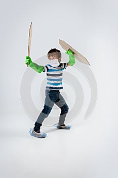 Little caucasian boy as a warrior in fight with coronavirus pandemic, with a shield, a sword and a toilet paper