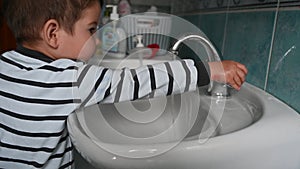 Little caucasian boy in bathroom turns off the water and shows his clean hands