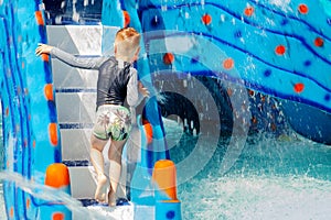 Little Caucasian boy with blond hair climbing the water slide in the children pool. Trickles of water everywhere, wet T-shirt and photo