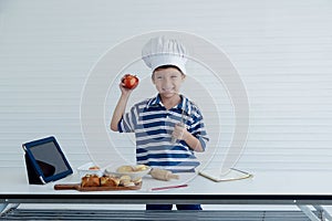 A little Caucasian boy chef with tablet to prepare food for cooking in studio kitchen